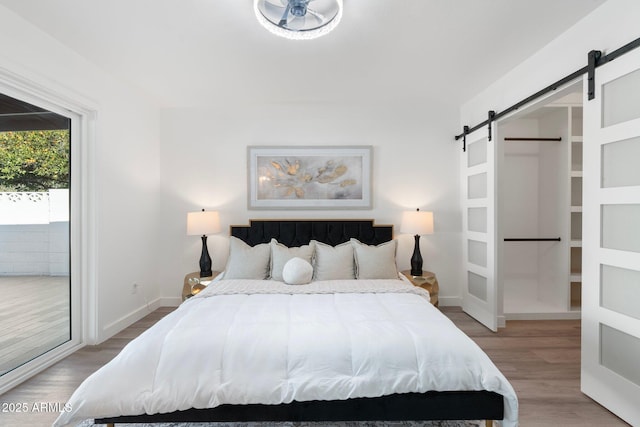 bedroom with wood-type flooring, a barn door, and access to outside