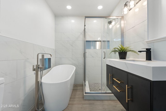 bathroom featuring independent shower and bath, vanity, wood-type flooring, and tile walls