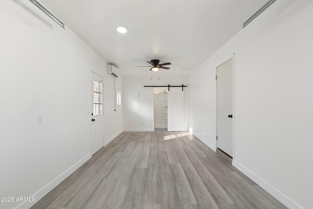 empty room featuring light hardwood / wood-style flooring, a wall unit AC, a barn door, and ceiling fan