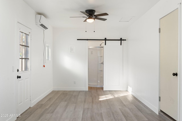 unfurnished room featuring light hardwood / wood-style floors, an AC wall unit, ceiling fan, and a barn door