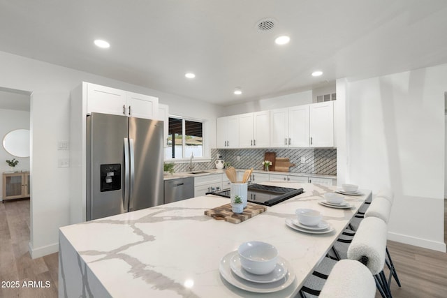 kitchen featuring stainless steel appliances, light stone counters, light hardwood / wood-style floors, white cabinets, and decorative backsplash