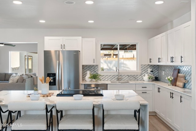 kitchen with white cabinets, a breakfast bar, stainless steel fridge, and light stone counters