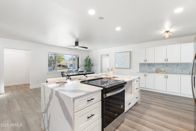 kitchen with white cabinetry, stainless steel electric range oven, a center island, and light wood-type flooring