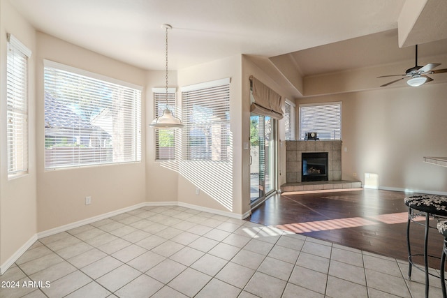 dining area with ceiling fan, a tiled fireplace, a wealth of natural light, and light hardwood / wood-style flooring