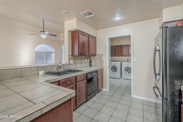 kitchen with tile counters, sink, black dishwasher, washing machine and dryer, and fridge