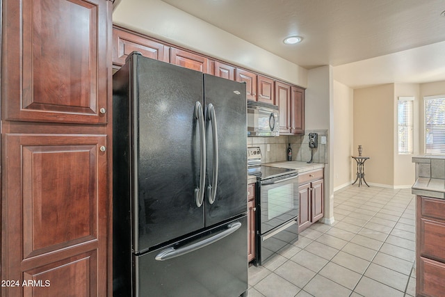 kitchen featuring range with electric stovetop, decorative backsplash, black fridge, and light tile patterned floors