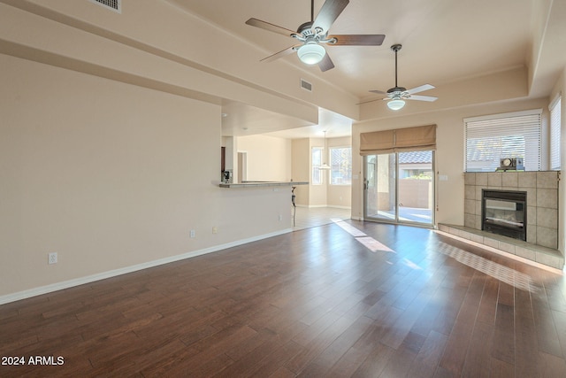 unfurnished living room with ceiling fan, wood-type flooring, and a tiled fireplace