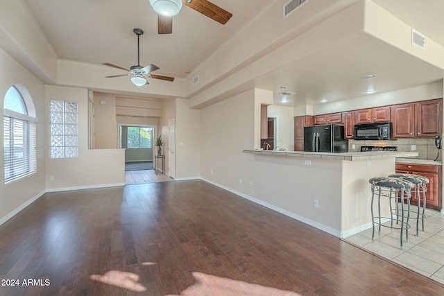 kitchen featuring a breakfast bar area, light hardwood / wood-style flooring, black appliances, and plenty of natural light