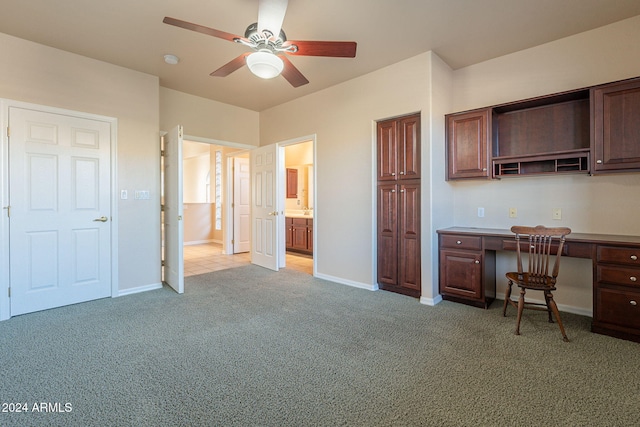 unfurnished office featuring light carpet, ceiling fan, and built in desk