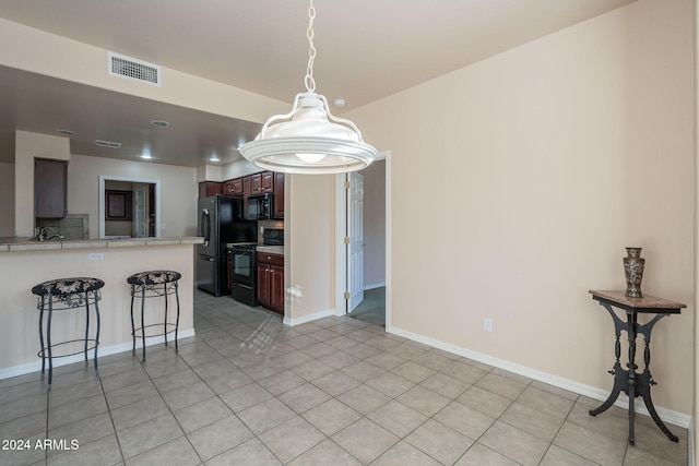 kitchen featuring kitchen peninsula, a breakfast bar, light tile patterned floors, and black appliances