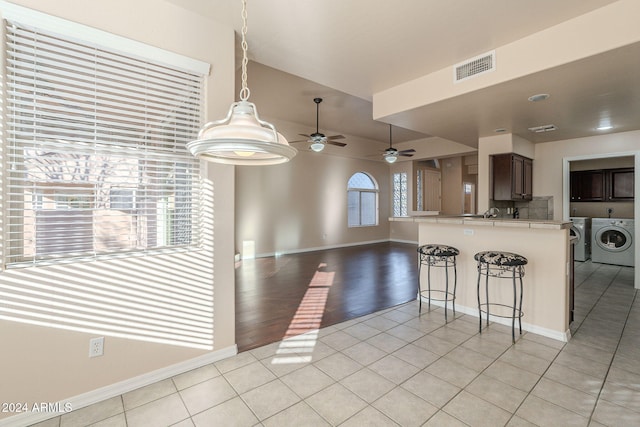 kitchen featuring a breakfast bar, light hardwood / wood-style flooring, ceiling fan, dark brown cabinets, and washing machine and clothes dryer