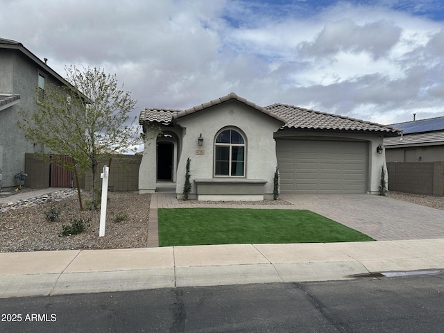 mediterranean / spanish-style house featuring fence, stucco siding, a garage, a tile roof, and decorative driveway