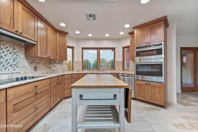 kitchen featuring sink, a center island, tasteful backsplash, light stone counters, and appliances with stainless steel finishes