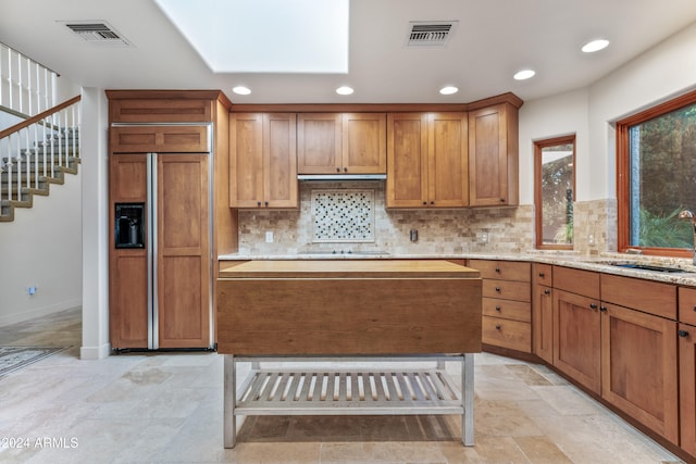 kitchen with paneled refrigerator, backsplash, light stone counters, and sink