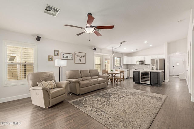 living area with a ceiling fan, beverage cooler, dark wood finished floors, lofted ceiling, and visible vents