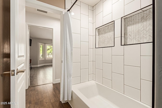 bathroom with shower / bath combo, baseboards, hardwood / wood-style floors, and visible vents