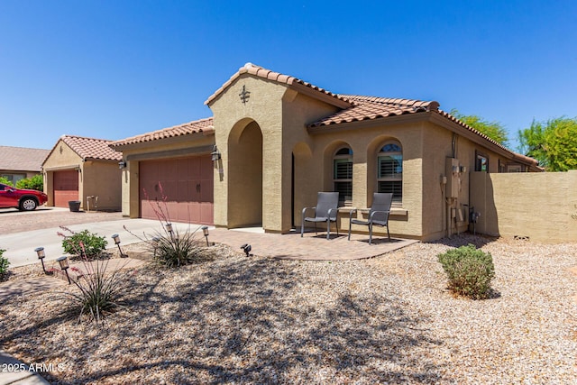 mediterranean / spanish home with a garage, a tiled roof, concrete driveway, and stucco siding