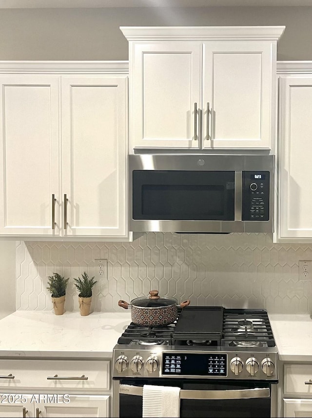 kitchen with decorative backsplash, light stone countertops, white cabinets, and appliances with stainless steel finishes