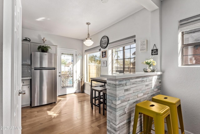 kitchen featuring light hardwood / wood-style flooring, gray cabinets, stainless steel refrigerator, hanging light fixtures, and a kitchen bar