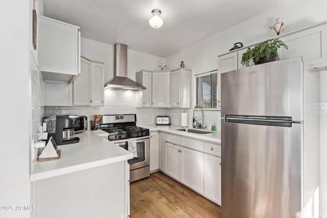 kitchen with wall chimney range hood, sink, white cabinetry, backsplash, and stainless steel appliances