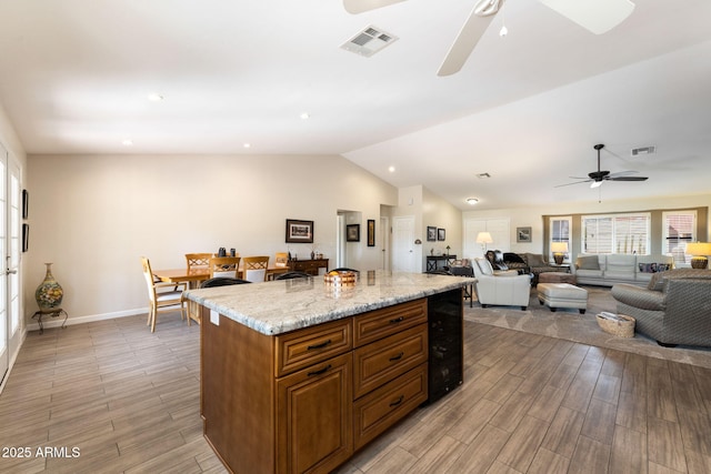 kitchen featuring ceiling fan, light stone counters, beverage cooler, and a center island