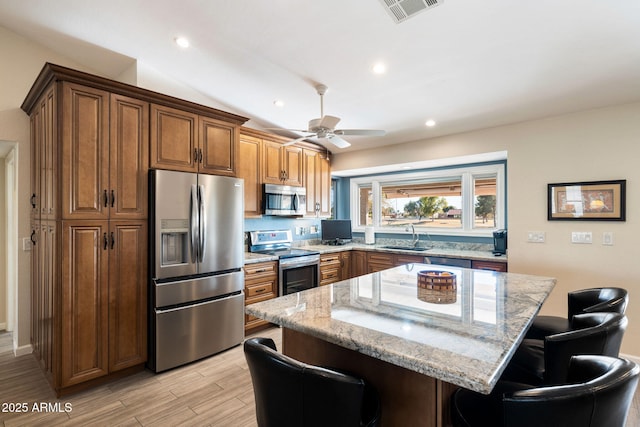 kitchen featuring light stone countertops, appliances with stainless steel finishes, a center island, sink, and a breakfast bar