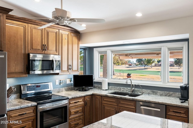 kitchen with ceiling fan, appliances with stainless steel finishes, lofted ceiling, light stone countertops, and sink