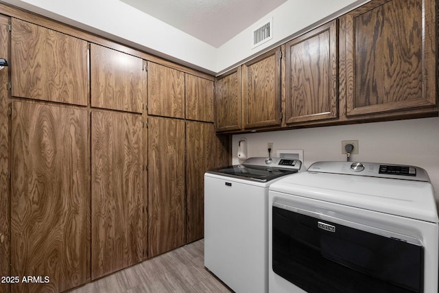 washroom with light wood-type flooring, cabinets, and washer and clothes dryer