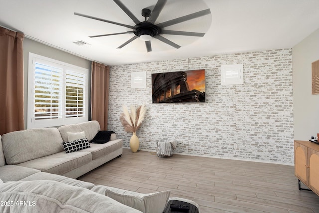 living room featuring wood finished floors, visible vents, brick wall, and ceiling fan