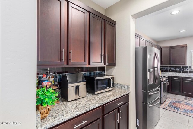 kitchen featuring light tile patterned flooring, stainless steel appliances, recessed lighting, light stone counters, and backsplash