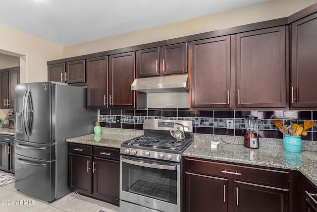 kitchen with light stone counters, under cabinet range hood, light tile patterned floors, stainless steel appliances, and decorative backsplash