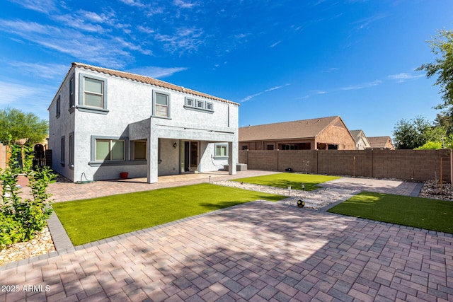 back of house with a fenced backyard, stucco siding, a patio, and a yard