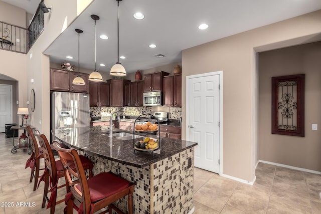 kitchen featuring decorative light fixtures, sink, dark stone countertops, a kitchen breakfast bar, and stainless steel appliances