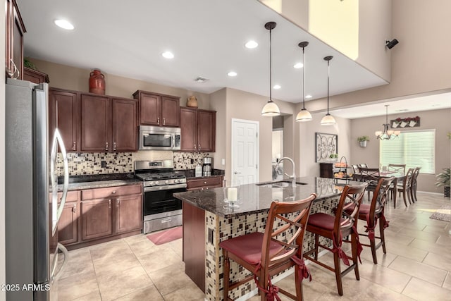 kitchen with sink, a center island with sink, dark stone countertops, pendant lighting, and stainless steel appliances