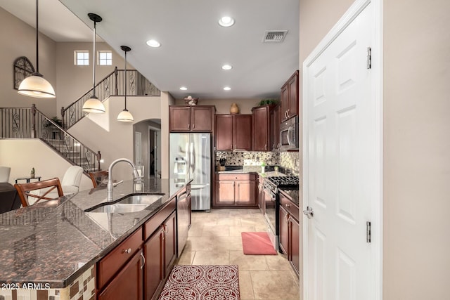 kitchen with appliances with stainless steel finishes, decorative light fixtures, tasteful backsplash, sink, and dark stone counters