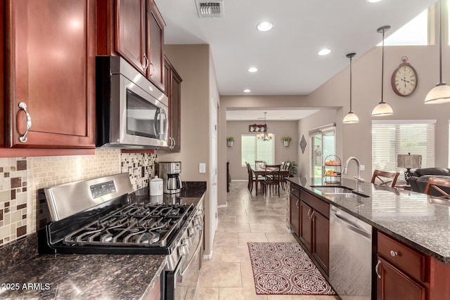 kitchen with appliances with stainless steel finishes, decorative light fixtures, sink, dark stone countertops, and decorative backsplash