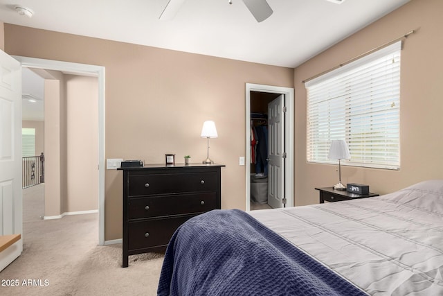 bedroom with a walk in closet, light colored carpet, ceiling fan, and a closet