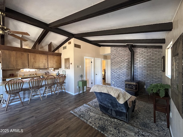 living area featuring lofted ceiling with beams, dark wood-style flooring, visible vents, baseboards, and a wood stove