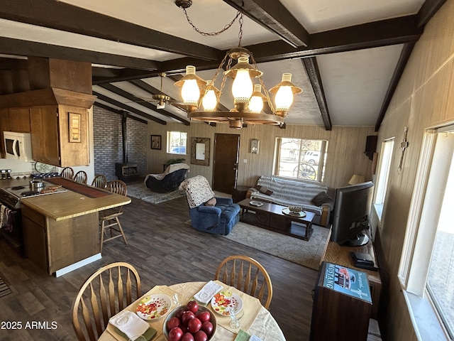 dining space featuring vaulted ceiling with beams, dark wood-style floors, a wood stove, and an inviting chandelier