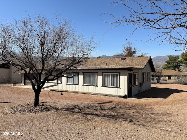 view of side of home with a shingled roof and a mountain view