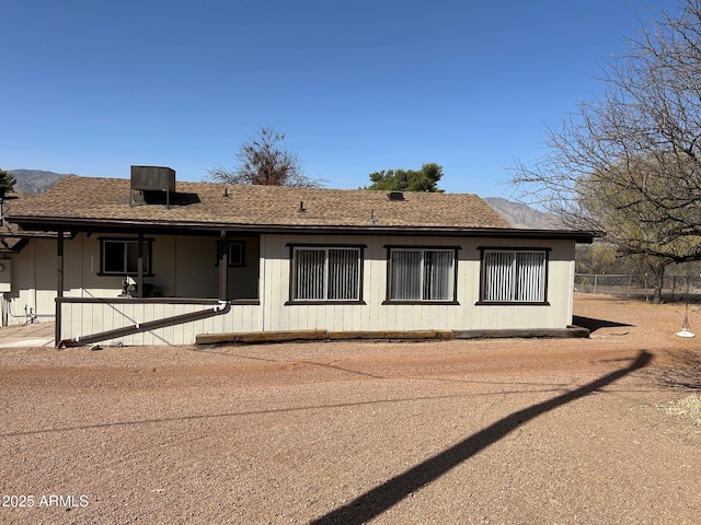 view of front of house with a patio area, a shingled roof, fence, and cooling unit