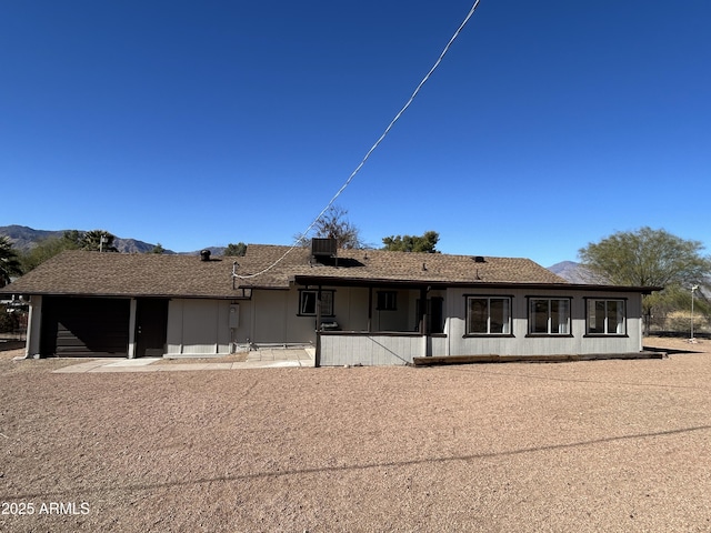 view of front facade with an attached garage, a shingled roof, central AC unit, and a mountain view