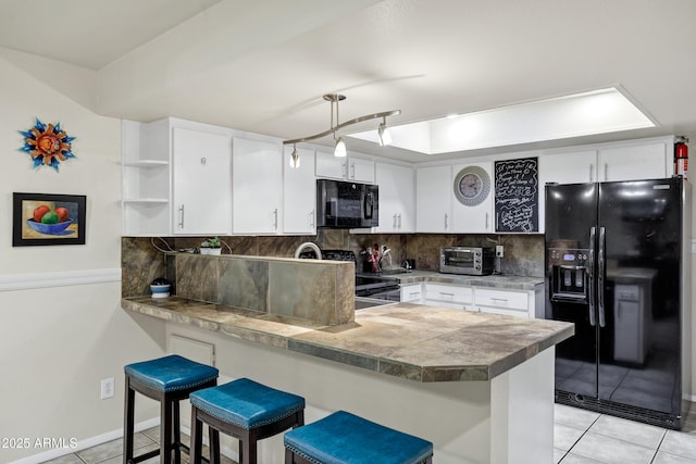 kitchen with light tile patterned flooring, a kitchen bar, black appliances, kitchen peninsula, and white cabinets