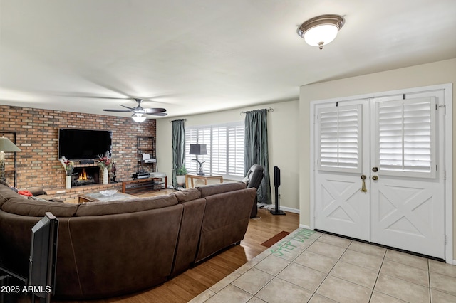 living room with ceiling fan, brick wall, a fireplace, and light hardwood / wood-style flooring