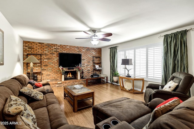 living room with ceiling fan, brick wall, a fireplace, and light hardwood / wood-style floors