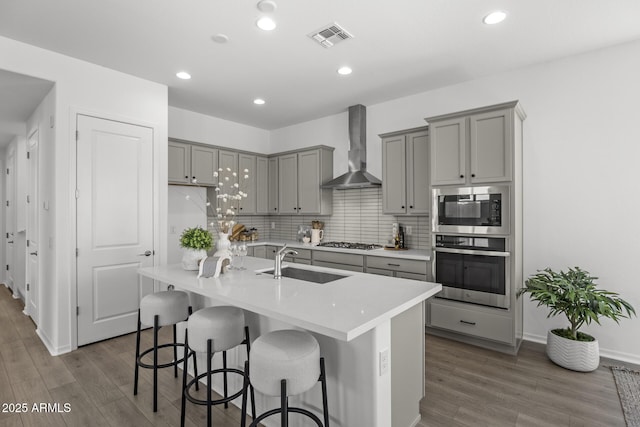 kitchen with visible vents, gray cabinets, a sink, appliances with stainless steel finishes, and wall chimney range hood