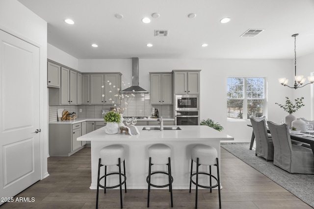 kitchen with a sink, stainless steel appliances, gray cabinetry, and wall chimney exhaust hood