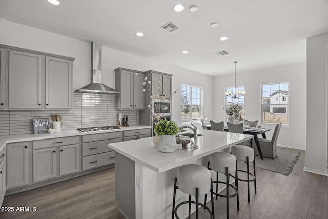 kitchen featuring wall chimney range hood, visible vents, gray cabinets, and stainless steel appliances