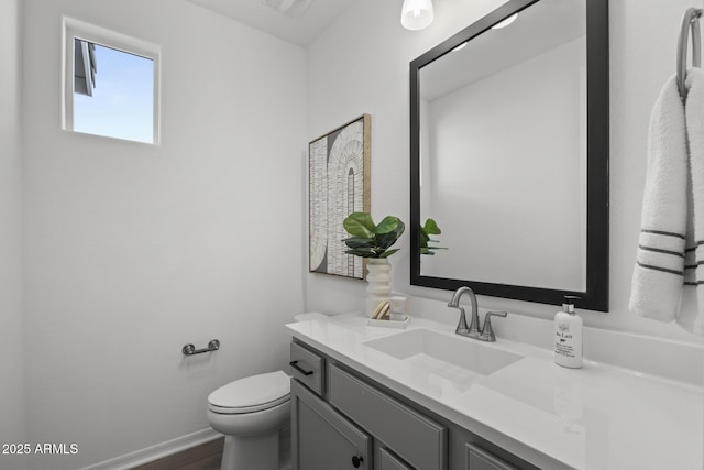 half bathroom featuring baseboards, toilet, and vanity