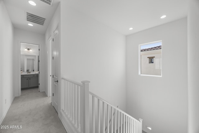 hallway with visible vents, recessed lighting, a sink, light carpet, and an upstairs landing